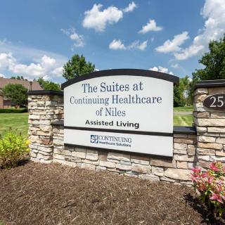 A sign for The Suites at Continuing Healthcare of Niles set outdoors against a blue sky.