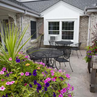 A cozy patio with colorful flowers, tables, and chairs.