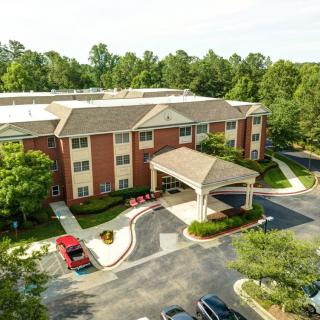 Aerial view of a brick hotel building surrounded by trees with a parking lot in front.