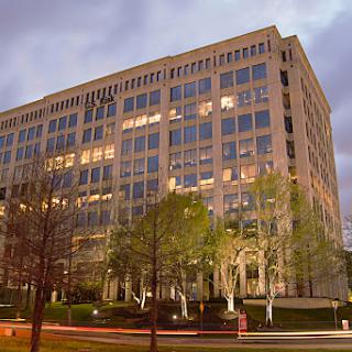 A modern office building illuminated at dusk, surrounded by greenery.