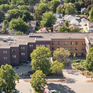 Aerial view of a residential building surrounded by trees and a parking lot in a neighborhood setting.
