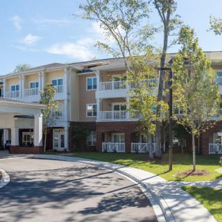 A modern residential building with a welcoming entrance, surrounded by trees, under a clear blue sky.