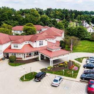An aerial view of a hotel with a red roof, surrounded by greenery and parked cars.