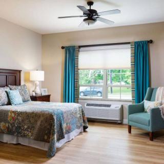 A cozy bedroom with a large bed, blue curtains, and an armchair by the window.