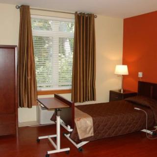 A hospital room with a single bed, bedside table, and a window with curtains.