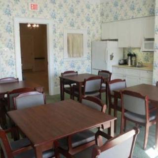 A dining area with several wooden tables and chairs, set next to a small kitchen with appliances.