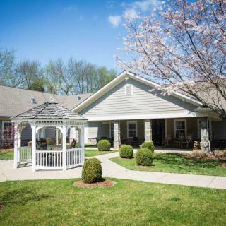 A pleasant house with a white gazebo and manicured lawn surrounded by trees in full bloom.
