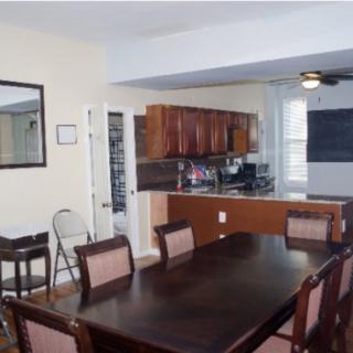 A dining room with a dark wooden table and chairs, adjoining an open-plan kitchen.