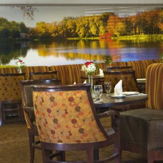 A cozy restaurant dining area featuring comfortable seating and a scenic wall mural of a lake.
