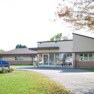 A small clinic building with a driveway and trees in the foreground on a clear day.