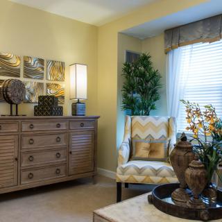 A cozy living room with elegant decor, featuring a dresser, a patterned armchair, and indoor plants.