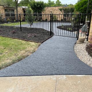 A newly paved concrete pathway leading to a fenced area in a landscaped garden.
