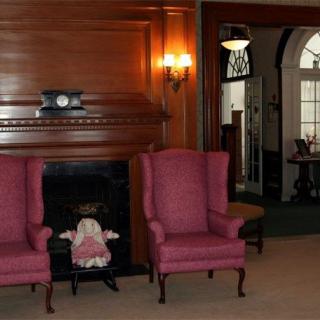 A traditionally decorated room with a fireplace, two armchairs, and a doll placed between them.