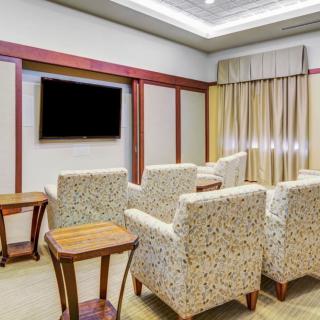 A cozy living room with patterned chairs arranged around a television, complemented by wooden side tables and elegant curtains.