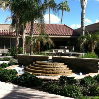 A serene courtyard featuring a tiered fountain surrounded by lush palm trees and well-maintained landscaping.