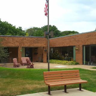 A serene outdoor seating area with a bench and a flagpole outside a brick building.