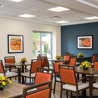 A modern dining room with orange chairs and floral centerpieces, featuring artwork on the walls.