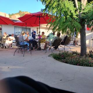 A lively outdoor dining area with people enjoying their meals under red umbrellas on a sunny day.