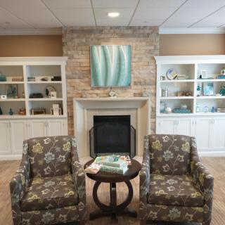 A cozy living room with a stone fireplace, two patterned chairs, and built-in bookshelves.
