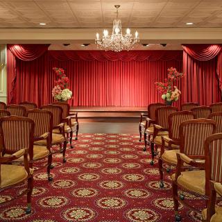 A luxurious auditorium with ornate seating and red curtains, featuring a chandelier overhead.
