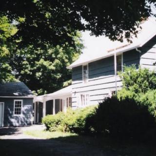 A residential house surrounded by trees and bushes under a clear sky.
