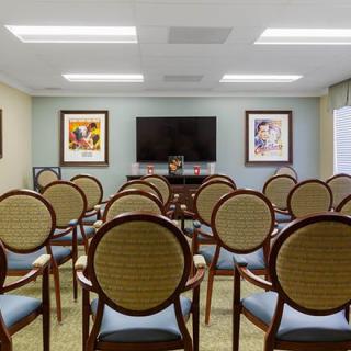 A small conference room with neatly arranged chairs facing a television and two paintings on the wall.
