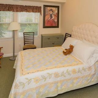 A cozy bedroom with a neatly made bed featuring a teddy bear, a lamp, and simple decor.