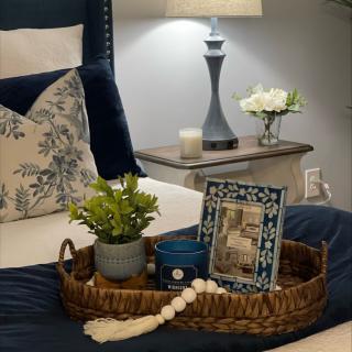 A cozy bedroom scene featuring a stylish tray with decor items, including a plant and picture frame, beside a softly lit lamp on the nightstand.