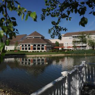 A serene view of a lakeside building reflecting in the calm waters, surrounded by lush greenery.