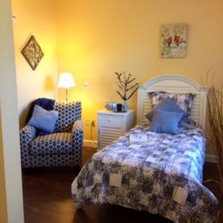 A cozy bedroom with a single bed and an armchair, warmly lit by a lamp.