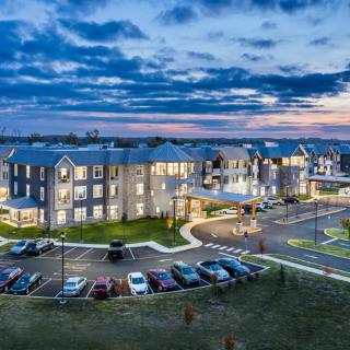 An illuminated apartment complex at dusk with a parking lot and a cloudy sky.