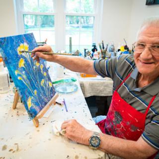 An elderly man enjoys painting a colorful flower scene on canvas, showcasing his creativity and passion for art.