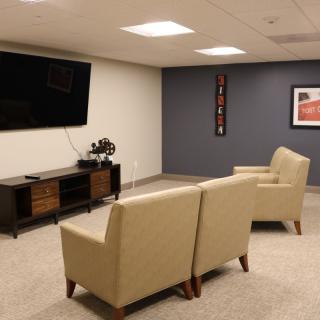 A modern living room with beige armchairs, a wall-mounted TV, and minimalist decor.