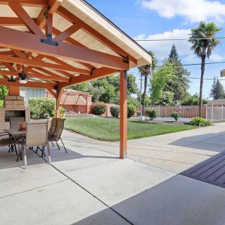 A spacious backyard with a covered patio area and outdoor dining set, surrounded by a well-maintained lawn and palm trees.