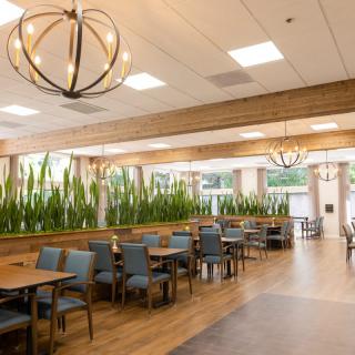 A modern restaurant interior with wooden flooring, stylish chandeliers, and blue chairs decorated with greenery.