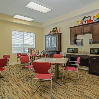 A bright and modern break room featuring red chairs, tables, and kitchen appliances.