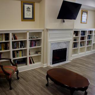 A cozy library setting featuring bookshelves, a fireplace, and comfortable seating.