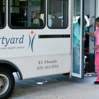 A person in a pink uniform boards a small bus labeled 'Courtyard' at a transit stop.