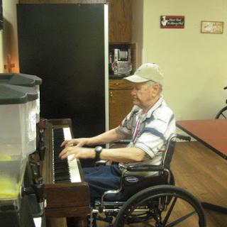 An elderly man enjoying a moment of music at the piano in a wheelchair.