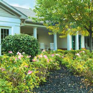 A beautifully landscaped front garden with blooming flowers and lush greenery in front of a house with white columns.