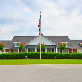A large building with a flagpole flying the American flag in front, surrounded by greenery under a cloudy sky.