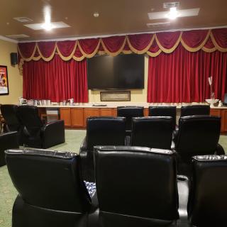 A cozy home theater setup with black leather seating and a large screen, framed by elegant red curtains.