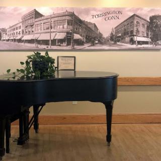 A black grand piano positioned near a historical mural, complemented by indoor plants.