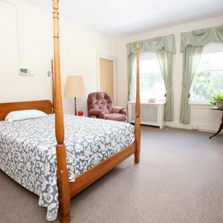 A spacious bedroom with a four-poster bed, an armchair, and large windows with green curtains.