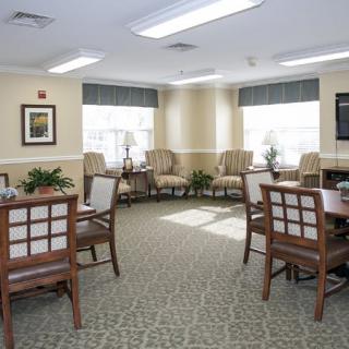 A well-lit seating area with tables and chairs, featuring large windows and indoor plants.