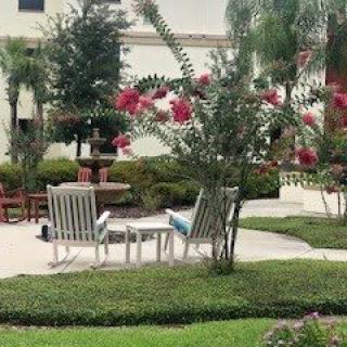 A tranquil garden setting with white chairs, vibrant flowers, and a fountain in the background.