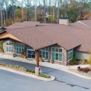 Aerial view of a modern commercial building surrounded by trees with a parking area in front.