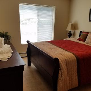 A cozy bedroom with a neatly made bed, wooden furniture, and soft lighting.