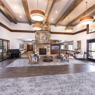 A spacious living room with a central stone fireplace, modern furniture, and wooden ceiling beams.