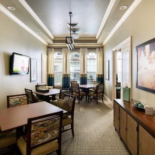 A well-lit dining area featuring multiple tables and chairs, decorated with elegant light fixtures and a wall-mounted television.